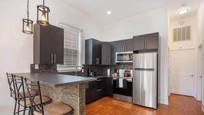 A modern kitchen with a central island, dark cabinetry, stainless steel appliances, and a bar stool seating area. - Spacious 4-Bed NOLA Home, Pet-Friendly (New Orleans)
