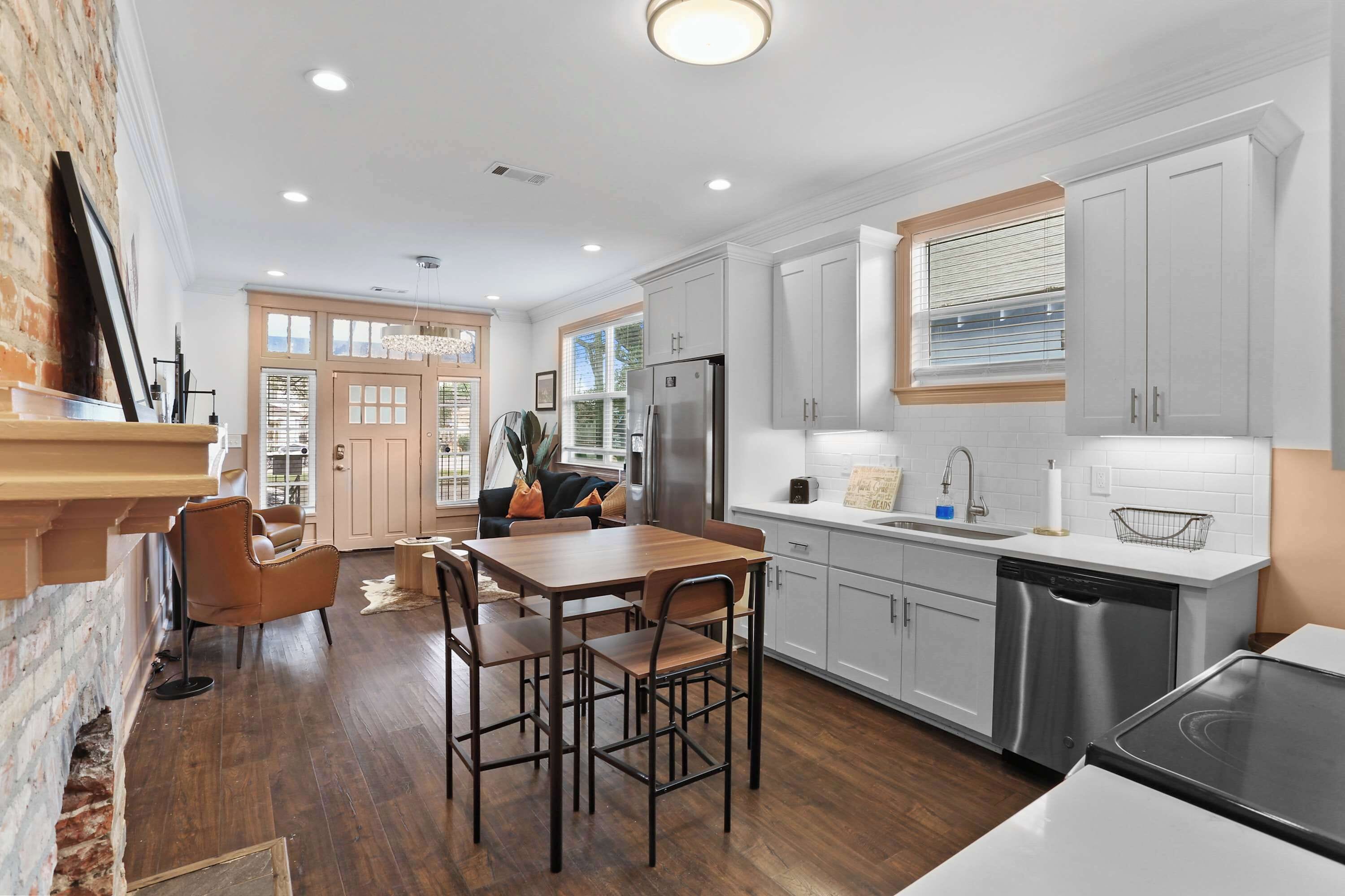 A modern kitchen with a dining area, featuring a brick wall, wooden flooring, and a large window.