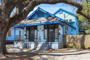 A two-story house with a blue exterior, a front porch with steps, and a wooden fence. - NOLA Charm: Free Parking (New Orleans)