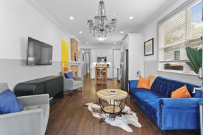 A modern living room with a blue sofa, a television, and a chandelier. - NOLA Charm: Free Parking (New Orleans)
