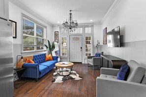 A living room with a blue sofa, a round coffee table, a chandelier, and a flat-screen TV mounted on the wall. - NOLA Charm: Free Parking (New Orleans)