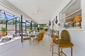 Un espace extérieur abrité, aménagé pour les repas, avec des meubles en osier, un ventilateur de plafond et une vue sur l’extérieur.