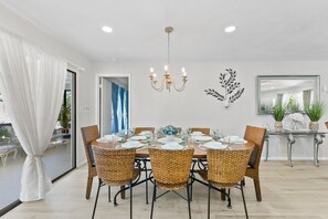 Ein Essbereich mit einem runden Tisch, gedeckt für sechs Personen, umgeben von Korbstühlen, einer Chandelierleuchtre und einem Wanddekor.