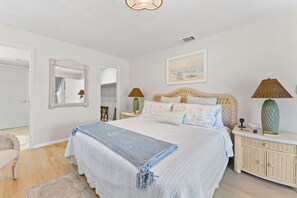 Um quarto com uma cama, mesas de cabeceira, um espelho, um quadro e um abajur.