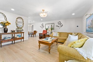 Ein helles Wohnzimmer mit Couch, Esstisch und Stühlen sowie einem Holztisch.