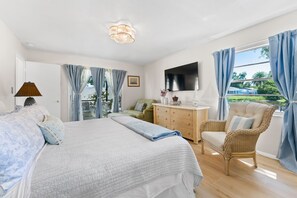 Ein Schlafzimmer mit einem Bett, einem Fernseher, einem Korbstuhl und Blick ins Freie.