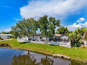 Ein Haus mit umzäunter Terrasse, einem kleinen Teich und üppiger Bepflanzung.