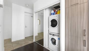 A laundry room with two stacked washing machines, a cabinet, and cleaning supplies on top.