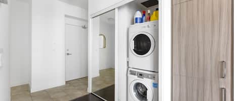 A laundry room with two stacked washing machines, a cabinet, and cleaning supplies on top.