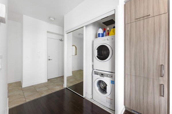 A laundry room with two stacked washing machines, a cabinet, and cleaning supplies on top.