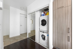 Un cuarto de lavado con dos lavadoras apiladas, un armario y productos de limpieza arriba.