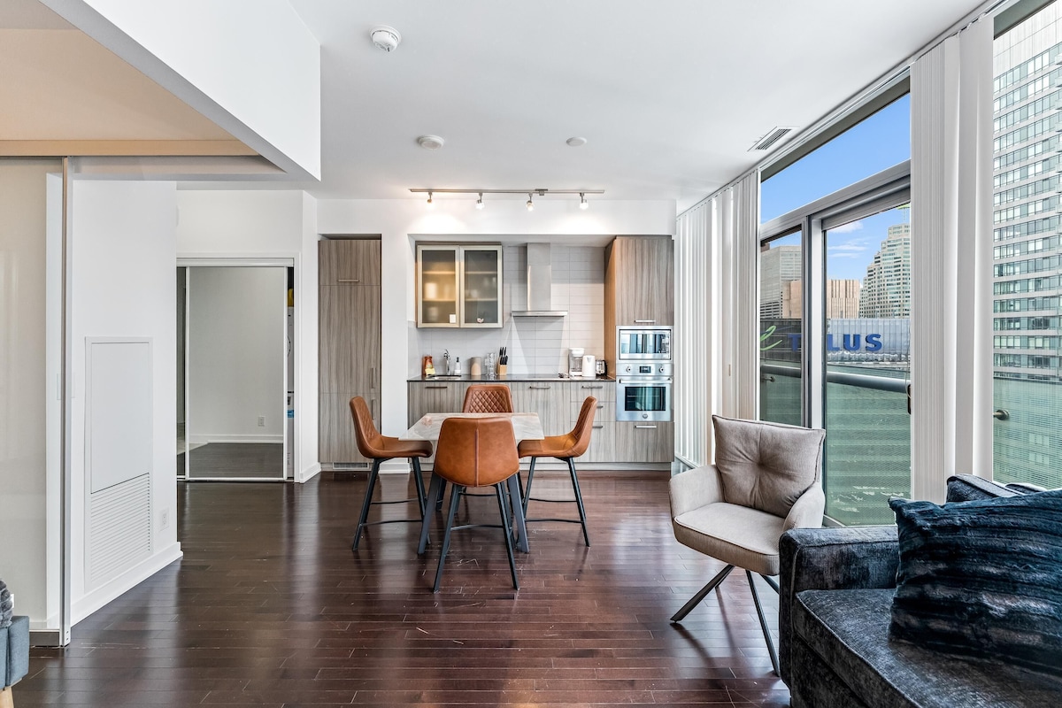 Un apartamento moderno con zona de comedor, cocina y ventanas amplias con vistas a la ciudad.