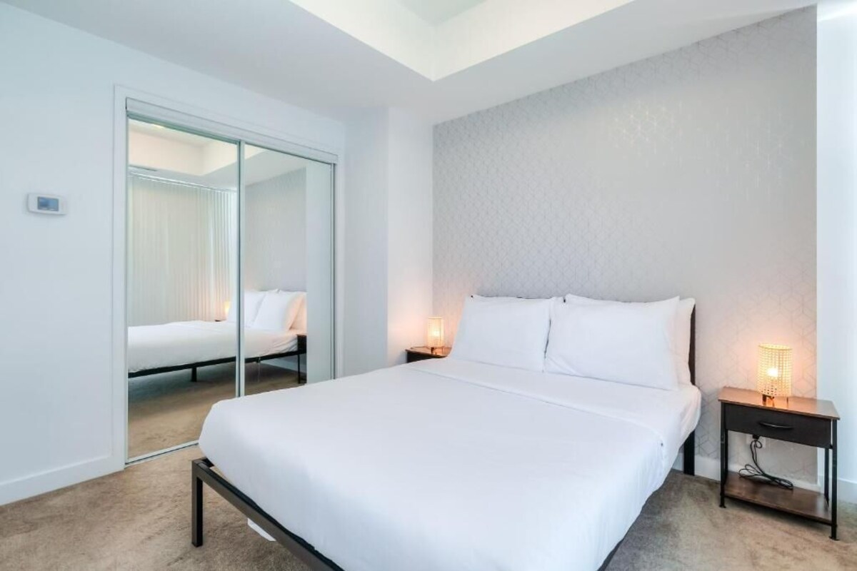 Een hotelkamer met een groot bed, een nachtkastje met een lamp, een spiegel en een schuifdeur naar een andere kamer.