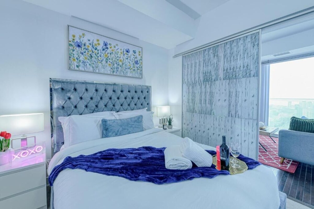 Een moderne hotelkamer met een groot bed, uitzicht over de stad, een neonbord en een balkon.