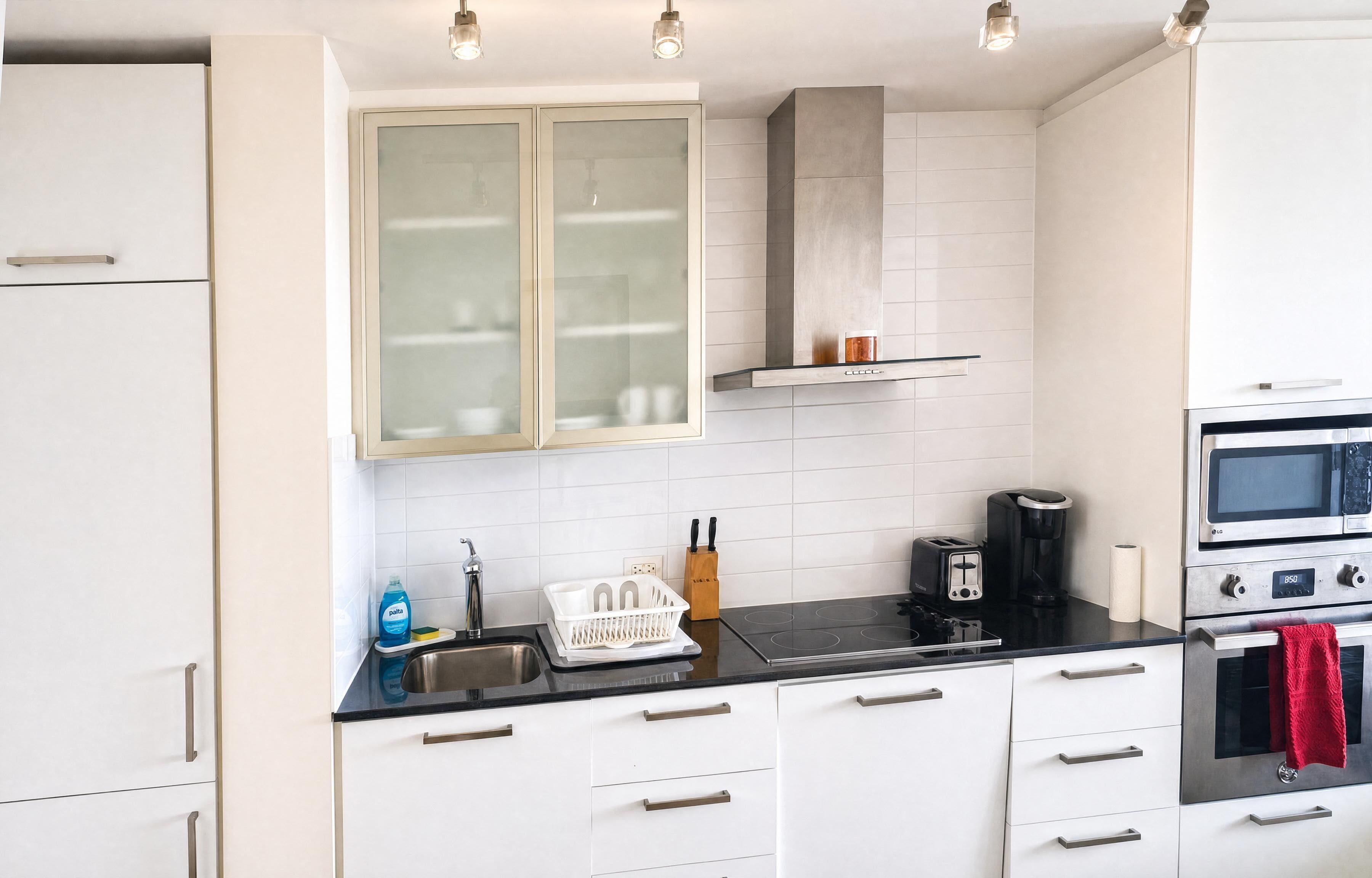 A modern kitchen with white cabinets, a black countertop, a built-in stove, and a stainless steel oven.