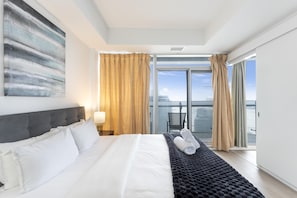 A hotel room with a large bed, a view of the city, and a balcony with curtains.