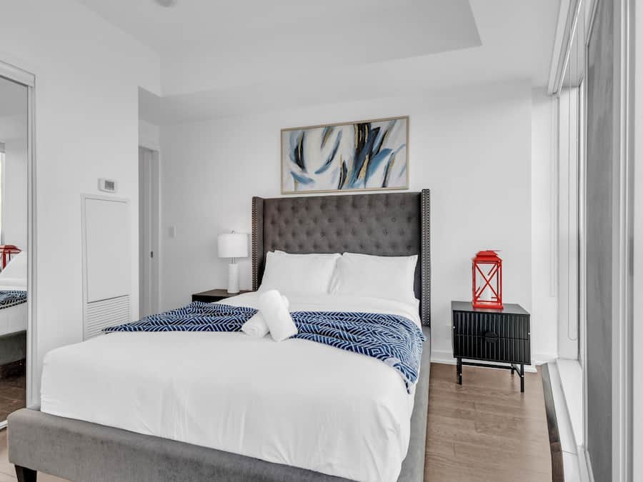 Una habitación de hotel moderna con una cama grande, un cabecero tapizado en gris, un farol rojo y un cuadro abstracto enmarcado en la pared.