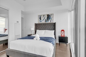 Een moderne hotelkamer met een groot bed, een grijs gestoffeerd hoofdeinde, een rode lantaarn en een abstract schilderij in een lijst aan de muur.