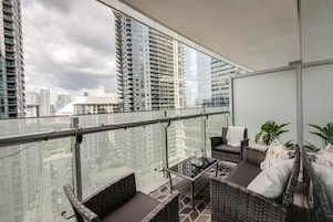 Een balkon met rieten meubilair, een glazen balustrade en uitzicht over de stad.
