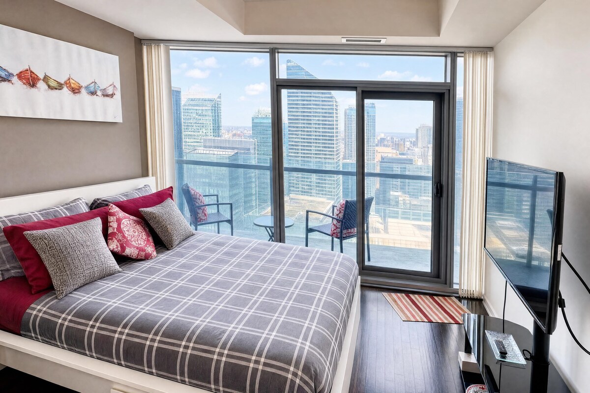 Habitación de hotel moderna con una cama grande, televisión, balcón con vistas al horizonte de la ciudad y una silla.