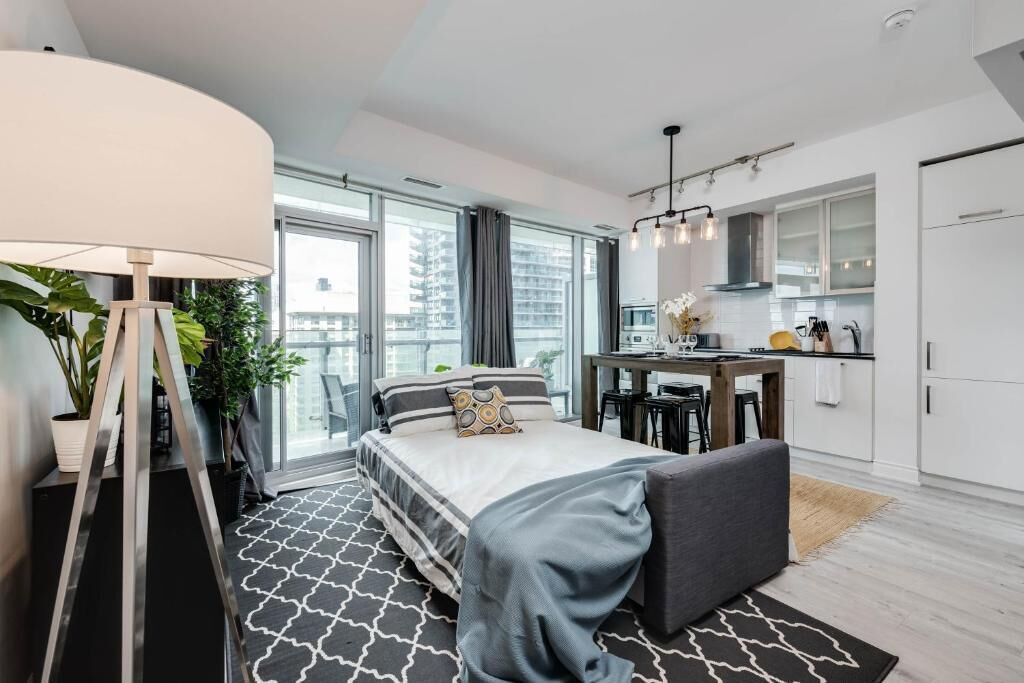 A modern hotel room with a large bed, a desk, a kitchenette, and a balcony with a view.