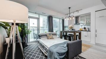 A modern hotel room with a large bed, a desk, a kitchenette, and a balcony with a view.