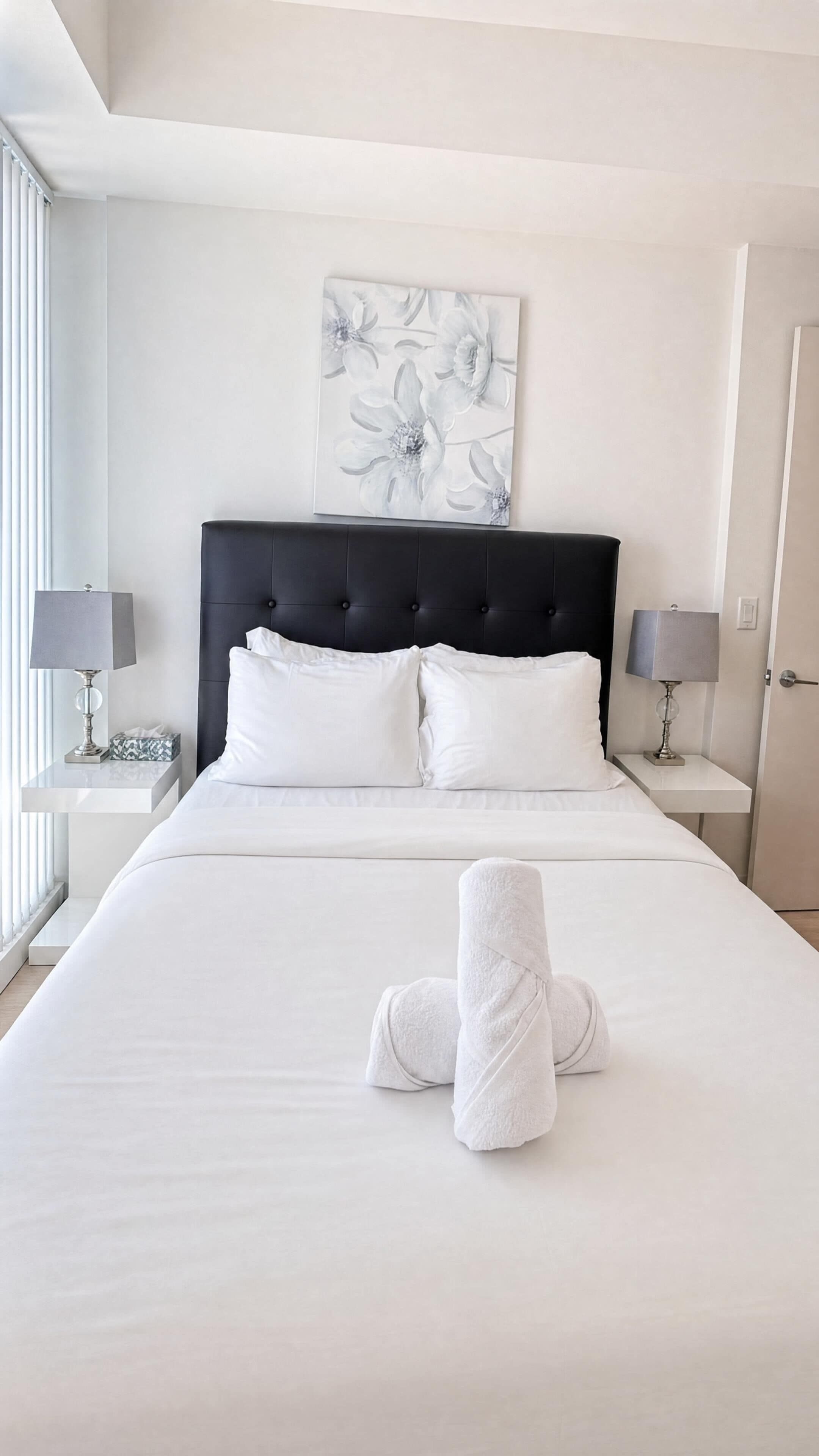 A neatly made bed with white linens, a black upholstered headboard, and two bedside lamps.