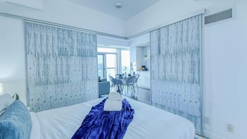 Ein modernes Schlafzimmer mit einem großen Bett, einer blauen Decke und Blick auf einen Essbereich.