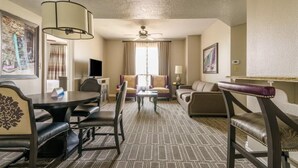 A hotel room with a dining table, two sofas, a coffee table, and a ceiling fan.