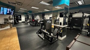 A gym with various exercise equipment, mirrors, and a television screen.