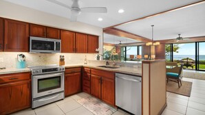 A modern kitchen with wooden cabinets, stainless steel appliances, and a view to the outdoors. - Poipu Kapili Condo 4 by Alekona Kauai - 2BR Oceanfront (Koloa)
