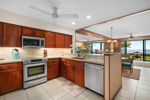 A modern kitchen with wooden cabinets, stainless steel appliances, and a view to the outdoors. - Poipu Kapili Condo 4 by Alekona Kauai - 2BR Oceanfront (Koloa)