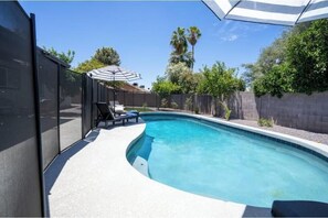 A swimming pool with a curved edge, surrounded by a concrete deck, a black fence, and a palm tree in the background. - 2-bedroom house in awesome Aguadilla with cool AC (Aguadilla)