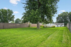 A well-maintained lawn with a large tree and a brick wall. - Cedar Grove Oasis:  Huge Private Yard + Gazebo (Cedar Rapids)
