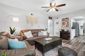 A modern living room with a brown leather sofa, a wooden coffee table, and a ceiling fan. - Cedar Grove Oasis:  Huge Private Yard + Gazebo (Cedar Rapids)