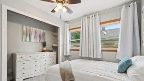 A bedroom with a bed, a dresser, a ceiling fan, a window with curtains, and a painting on the wall. - Cedar Grove Oasis:  Huge Private Yard + Gazebo (Cedar Rapids)