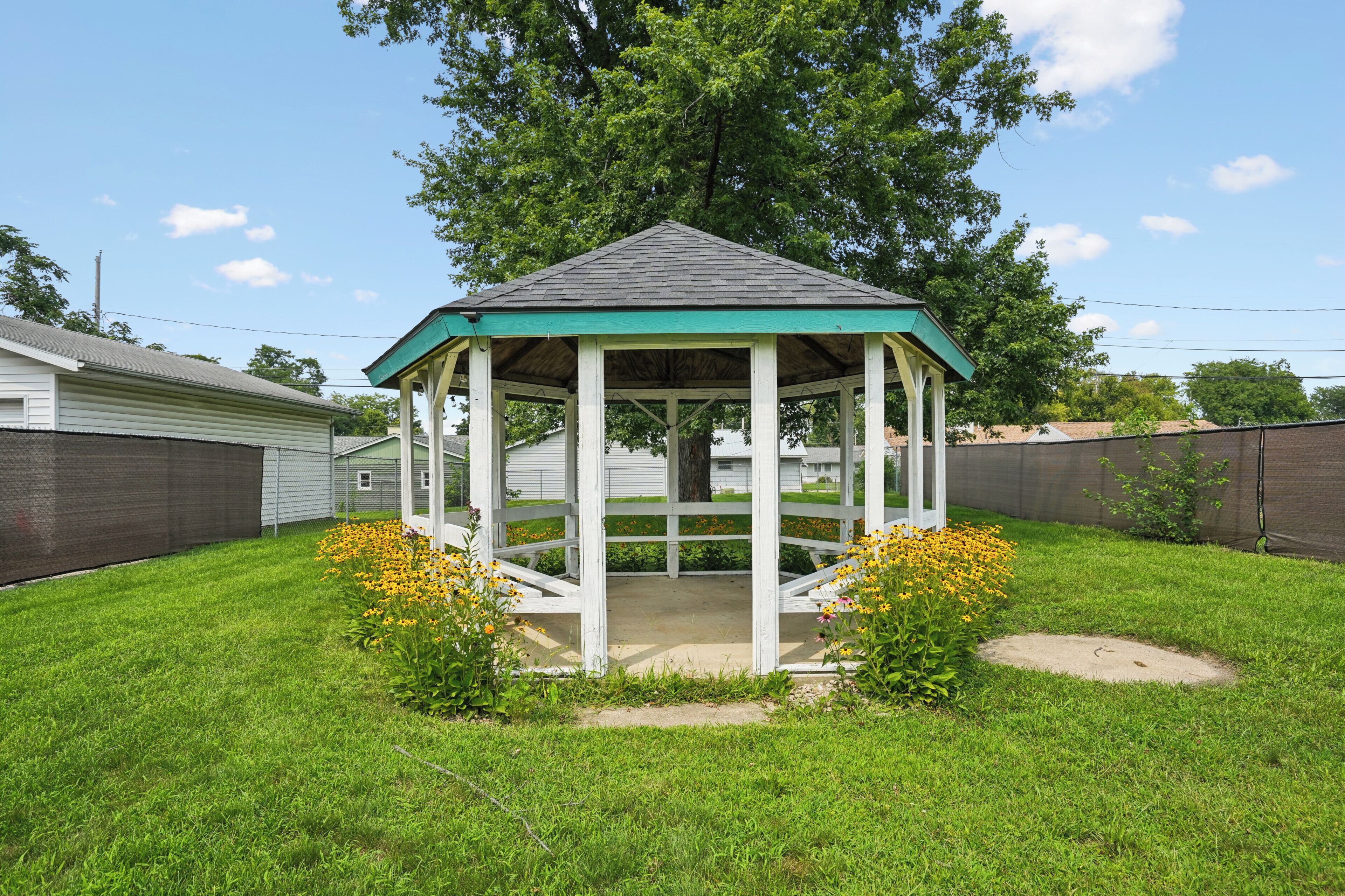 A gazebo with a green roof and white walls in a grassy backyard.
