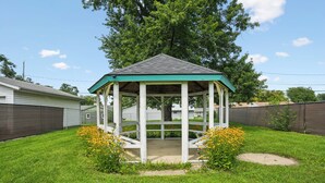 Un gazebo con techo verde y paredes blancas en un patio trasero cubierto de césped.