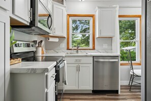 Eine moderne Küche mit weißen Schränken, einem eingebauten Backofen, einem Geschirrspüler und einem Fenster mit Blick auf Grünflächen.