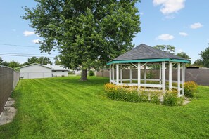 A gazebo with a green roof and white walls, surrounded by a well-maintained lawn and yellow flowers. - Cedar Grove Oasis:  Huge Private Yard + Gazebo (Cedar Rapids)