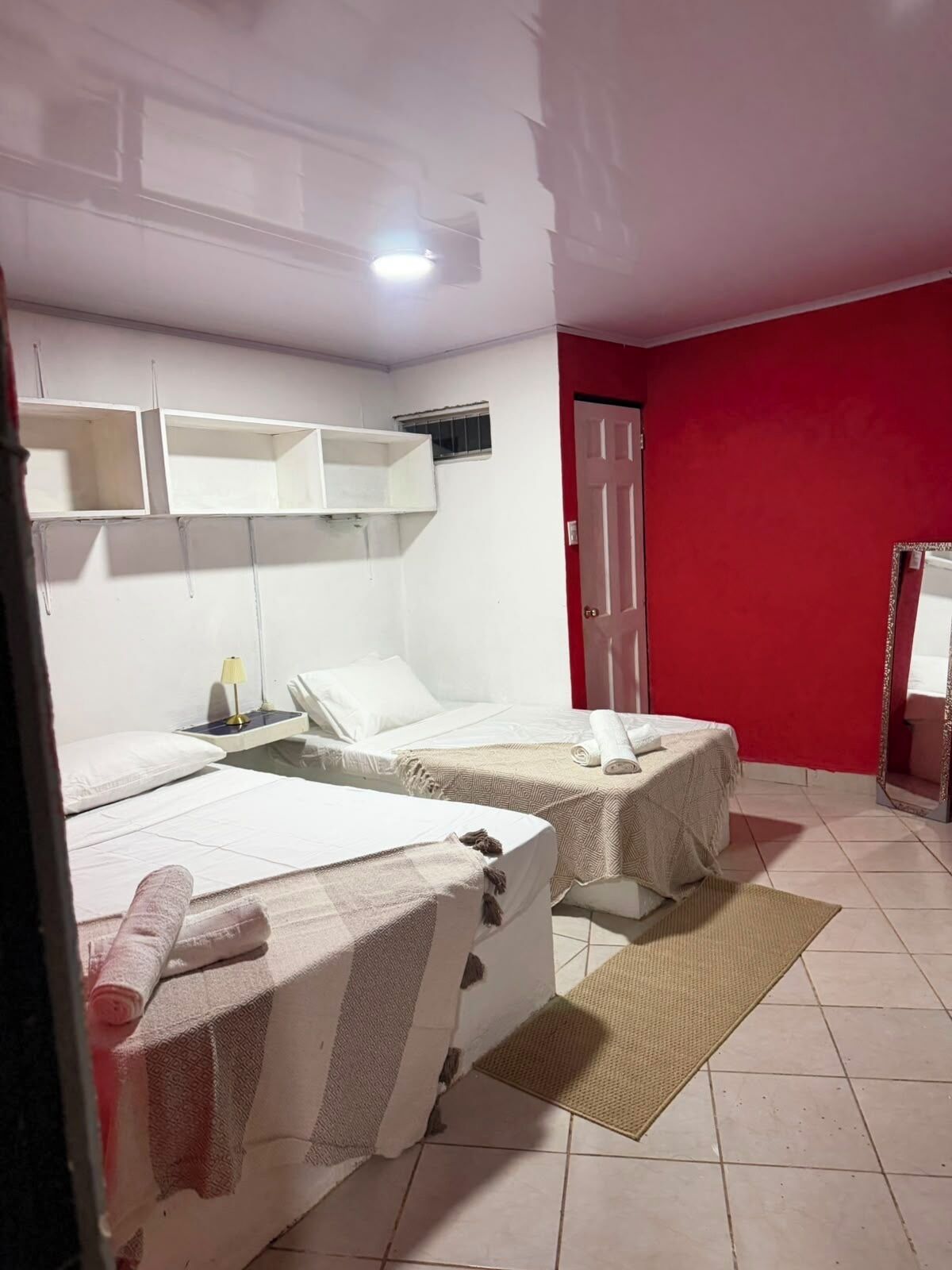 Habitación de hotel con dos camas, una pared de acento roja, un espejo y un ventanal pequeño.