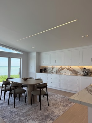 A modern kitchen with white cabinetry, a marble countertop, and a view of the sea.