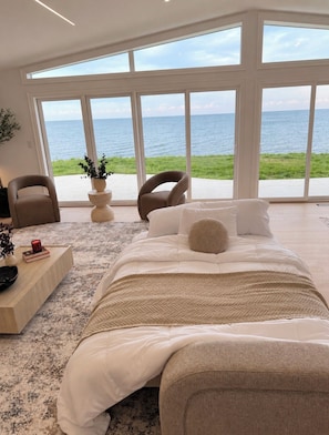 A bedroom with a large bed, two chairs, a coffee table, and a view of the sea.