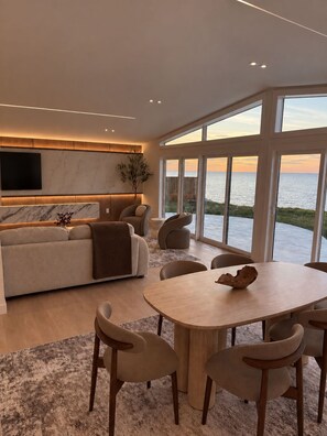A modern living room with a large window, a sofa, a dining table, and chairs.