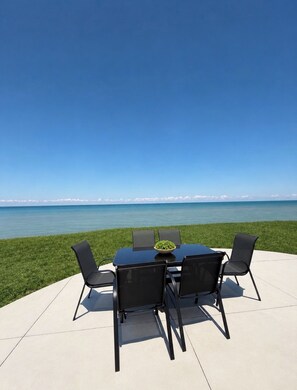 An outdoor dining area with a table and chairs overlooking a body of water.