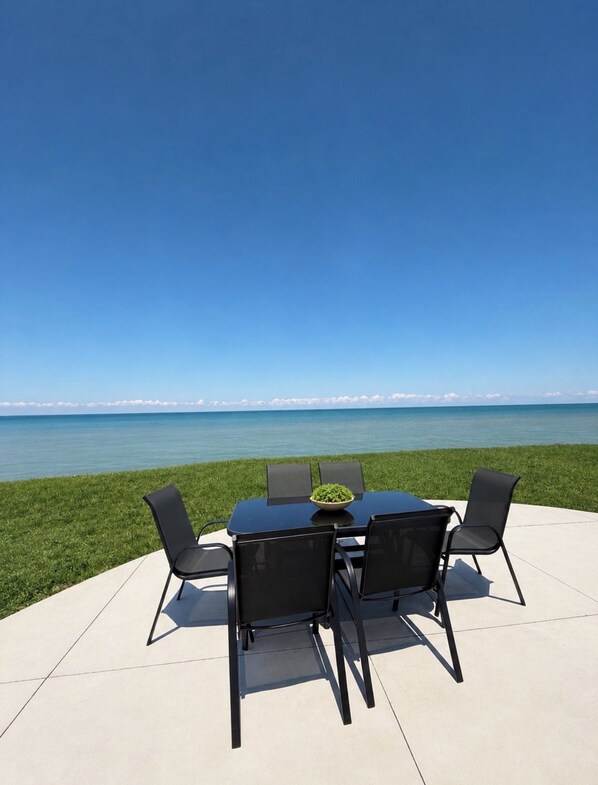 An outdoor dining area with a table and chairs overlooking a body of water.