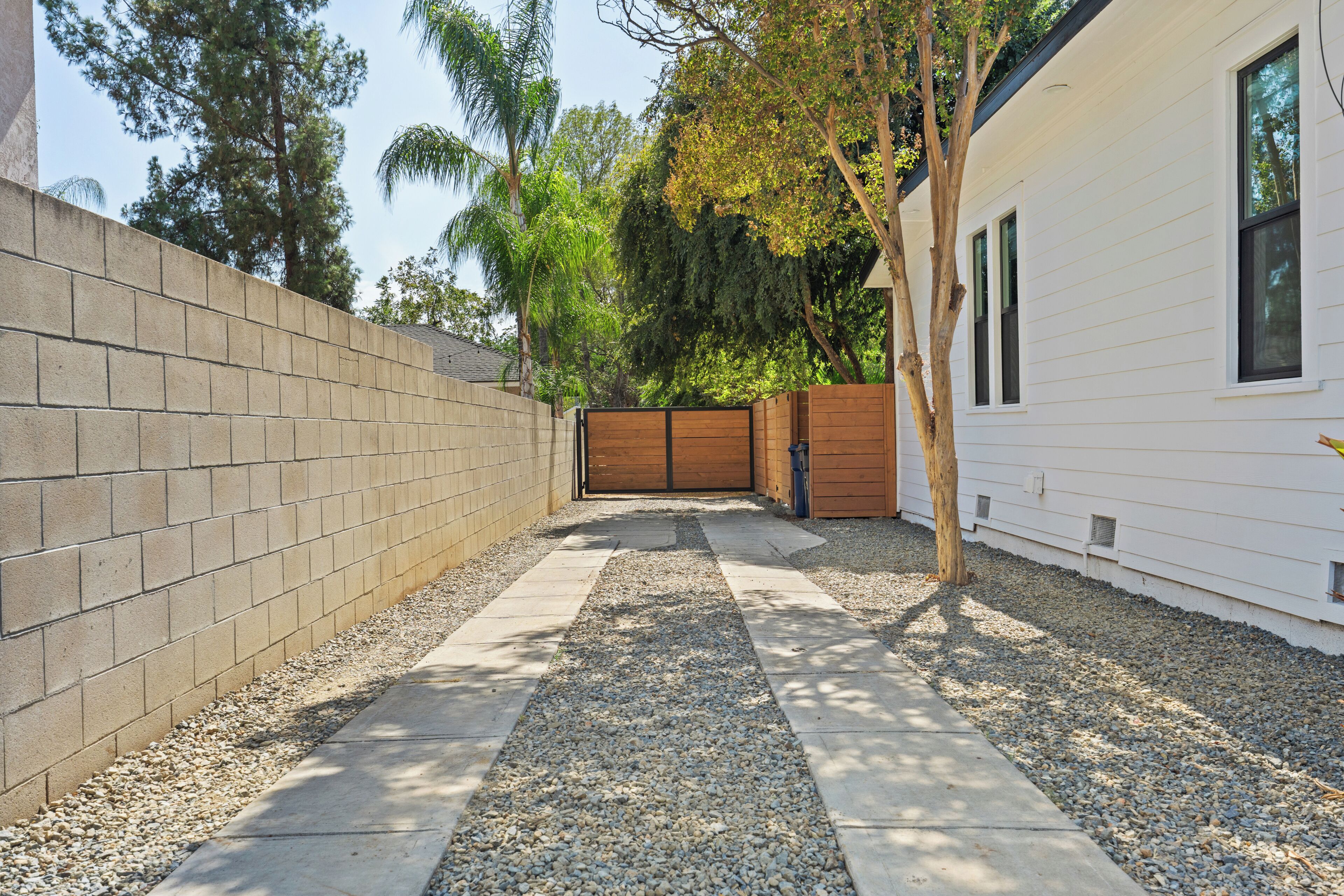 A pathway leading to a gated area with a white building on the right and a brick wall on the left.