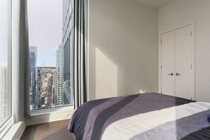 A bedroom with a large window, a bed with a striped bedspread, and a white wardrobe. - Rare luxury penthouse/P5 Executive Collection (Montréal)