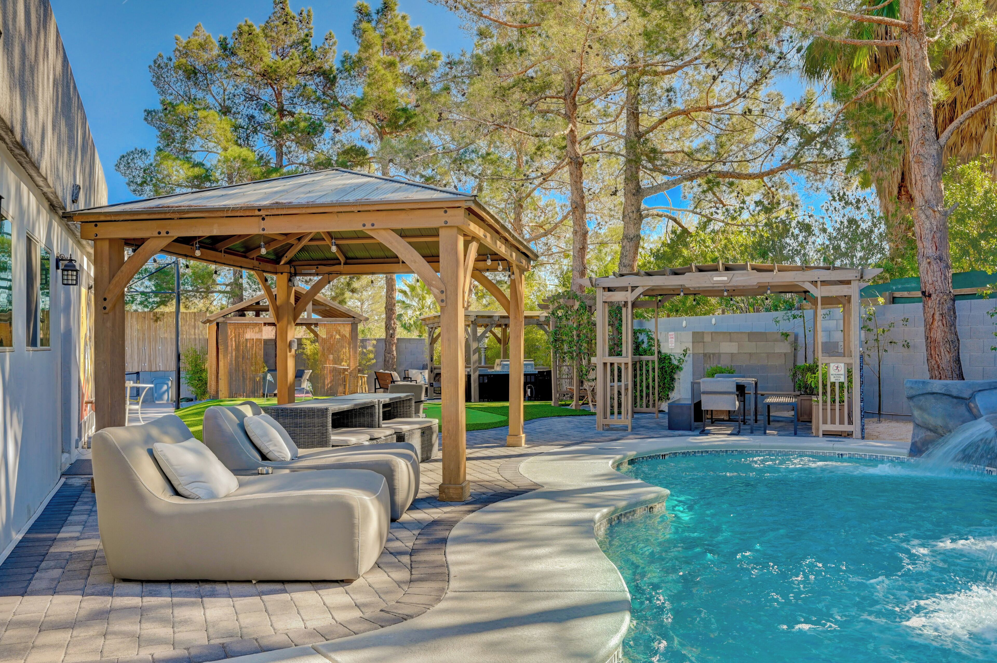 A pool area with a wooden pergola, lounge chairs, and a covered seating area.