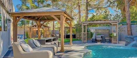 A pool area with a wooden pergola, lounge chairs, and a covered seating area.